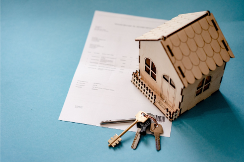 Small model house next to keyring with old style keys on top of contract paper